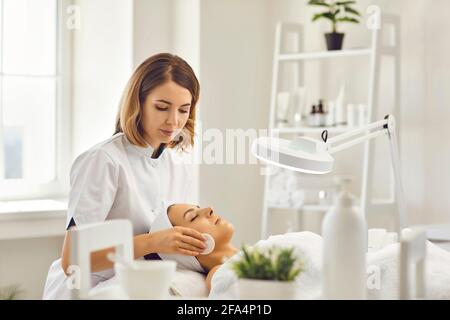 Junge Kosmetikerin oder Dermatologin, die das Gesicht der Frau mit Baumwolle reinigt Pads im Spa-Salon Stockfoto
