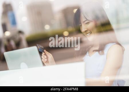 Asiatische Frau mit Kreditkarte mit Mobiltelefon und Technologie-Laptop für Online-Shopping in modernen Café, Technologie Geld Brieftasche und Online-pa Stockfoto
