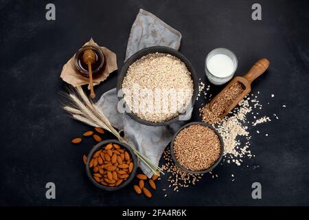 Gerollte Haferflocken in schwarzen Schalen und goldene Weizenohren auf dunklem Grund. Draufsicht Stockfoto