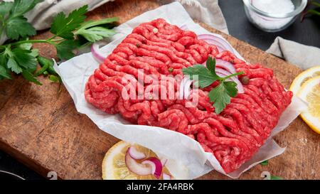 Rohes Hackfleisch mit Gewürzen, Gemüse und Kräutern auf dunklem Hintergrund. Zutaten für das Kochkonzept. Stockfoto