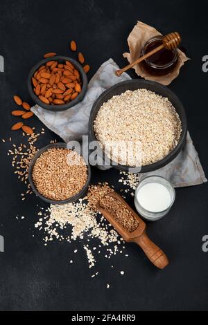 Gerollte Haferflocken in schwarzen Schalen und goldene Weizenohren auf dunklem Grund. Draufsicht Stockfoto
