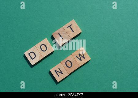 Do IT Now, Wörter in hölzernen Buchstaben auf grünem Hintergrund isoliert Stockfoto