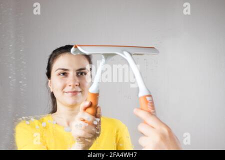 Die Putzfrau reinigt den Spiegel mit einem Wasserspender und Fensterreiniger. Hausreinigung. Reinigungsservice Stockfoto