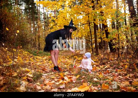 Frau Hexe spielt mit einem kleinen Kind im Herbstwald. halloween Konzept Kostüme. Hexe und Hase. Konzept der Freunde Mutter und Tochter Stockfoto