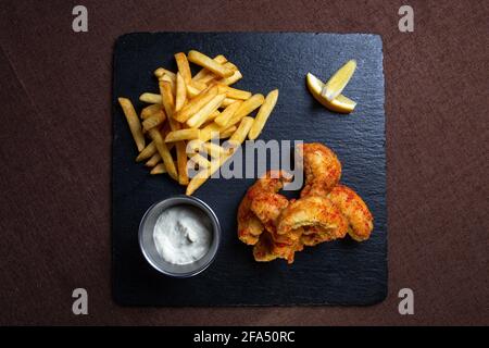 Fisch im Teig mit Pommes frites auf einem schwarzen Brett. Stockfoto