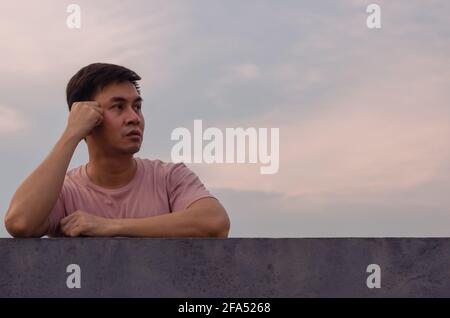 Asiatischer Mann bleibt allein mit Himmelshintergrund. Emotionsausdruck und Konzept der psychischen Gesundheit. Stockfoto