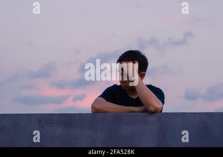 Asian miserable depressiven Mann bleiben allein mit Himmel Hintergrund. Depression und psychische Gesundheit Konzept. Stockfoto