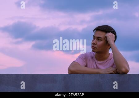 Asian miserable depressiven Mann bleiben allein mit Himmel Hintergrund. Depression und psychische Gesundheit Konzept. Stockfoto