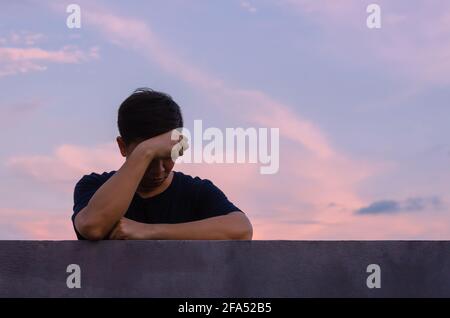 Asian miserable depressiven Mann bleiben allein mit Himmel Hintergrund. Depression und psychische Gesundheit Konzept. Stockfoto