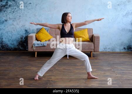 Frau in ihrem Wohnzimmer in Krieger-Yoga-Pose. Stockfoto