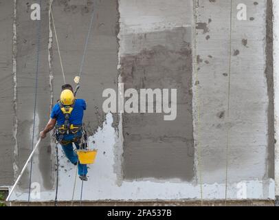 mason von Seilen mit Helm und Gurtzeug unterstützt, repariert die Außenwand eines Hauses Stockfoto