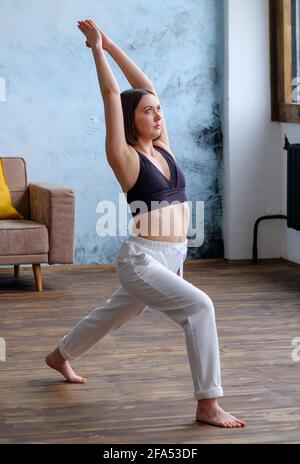 Frau in ihrem Wohnzimmer in Krieger-Yoga-Pose. Stockfoto