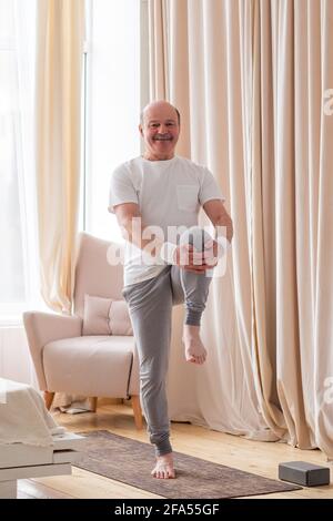 Seniorsportler, der zu Hause Stretching und Balancing Yoga macht. Wie man auf Quarantänekonzept gesund bleibt. Stockfoto