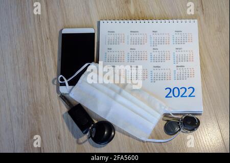 Telefon und Kalender 2022. Medizinische Maske und Kalender 2022. Schlüssel und Maske auf dem Schreibtisch. Stockfoto