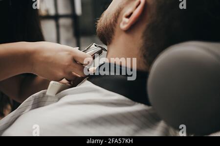 Mann mit Bart bekommt einen Haarschnitt mit einem elektrischen Maschine in einem Friseurladen Stockfoto