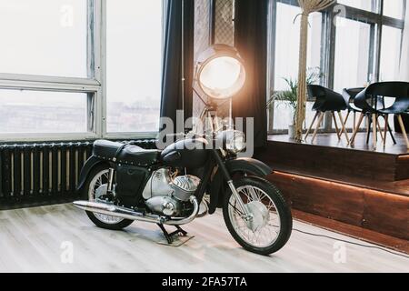 Altes Retro-Motorrad in einem Loft-Innenraum mit einem großen Lampe auf dem Hintergrund Stockfoto