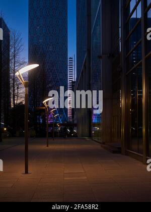 Ein Blick entlang einer leeren Straße, verlassen in der Dämmerung, umgeben von den Zyklopentürmen von Canary Wharf. Stockfoto