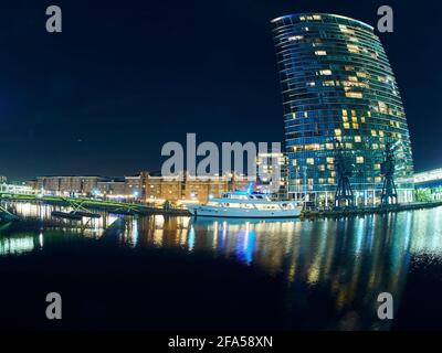 Ein Canary Wharf-Wolkenkratzer, von einer Fischaugenlinse verzerrt und mit lodernden Lichtern verzerrt, alles spiegelt sich in den stillen Gewässern des Docks wider. Stockfoto