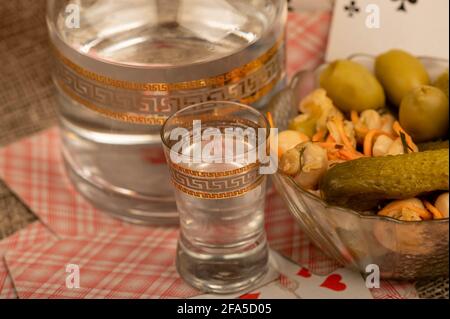 Spielkarten, ein Glas Wodka, ein Dekanter Wodka und eine Glasschale mit Gurken und Pilzen auf dem Tisch. Nahaufnahme, selektiver Fokus. Stockfoto