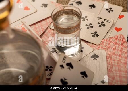 Spielkarten, ein Glas Wodka und ein Dekanter Wodka auf einem Tisch, der mit grobem Sackleinen bedeckt ist. Nahaufnahme, selektiver Fokus. Stockfoto