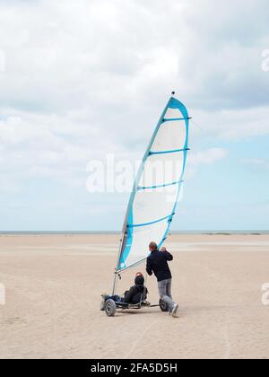 Sand Yacht Land Segeln am Strand Plage de Ouistreham in Frankreich. Ein Mann, der einer Yacht auf dem Sand hilft Stockfoto