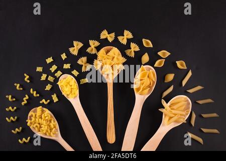 Verschiedene Nudelsorten in Holzlöffeln auf dem Tisch. Draufsicht. Rohpasta Kochkonzept. Stockfoto