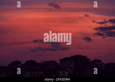 Schöner, roter, dramatischer Sonnenuntergang über einer kleinen Stadt in Bulgarien. Die hypnotisierenden roten und orangen Farben geben ein entspannendes und ruhiges Gefühl. Stockfoto