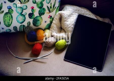 Garnkugeln zum Stricken. Garnkugeln zum Stricken in einem Korbkorb. Eine Tablette in der Nähe von Garnen für Mockup. Buntes mehrfarbiger Garn zum Stricken. Stockfoto