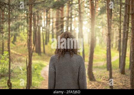 Frau von hinten, die mitten im Wald reflektiert. Meditiert in der Natur, denkt über den Weg nach vorne nach. Landschaft in einem Kiefernwald mit Sonnenuntergang Stockfoto