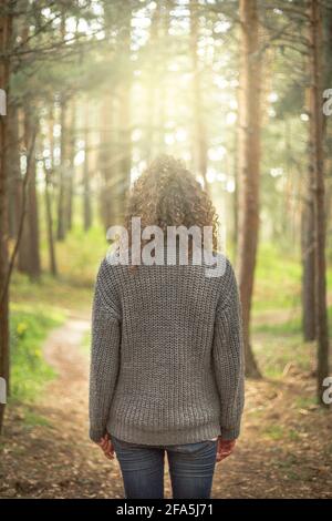 Frau von hinten, die mitten im Wald reflektiert. Meditiert in der Natur, denkt über den Weg nach vorne nach. Landschaft in einem Kiefernwald mit Sonnenuntergang Stockfoto