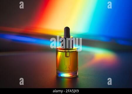 Gelbes Gesichtsöl mit einer Tropfflasche vor dem Hintergrund des Regenbogenprismas. Seitenansicht Stockfoto