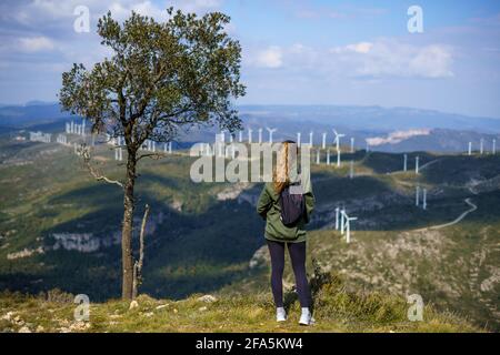 Rückansicht eines Weibchens auf einem Hügel Blick auf die Windkraftanlagen in den Bergen Stockfoto