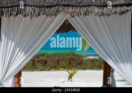 Ein eleganter Holzpavillon mit Reetdach und dekorativen Vorhängen an einem tropischen Strand auf Holbox Island in Mexiko. Stockfoto