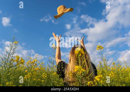 Glückliche junge Frau wirft ihren Strohsonnenhut in einem gelben Blumenfeld.Frühling Lifestyle, Sommer sonnigen Tag Konzept, kopieren Raum. Stockfoto