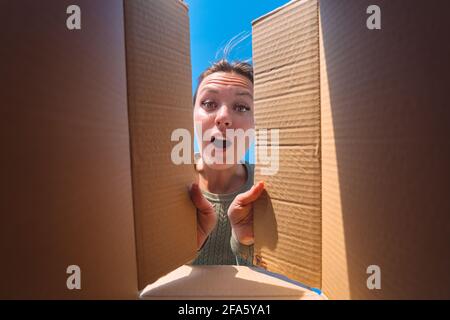 Überraschte Frau beim Auspacken des Pappkartons. Auspacken des Lieferpakets Stockfoto