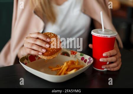 Mädchen hält EINEN Hamburger, Essen Fast Food und Trinken von Cola Stockfoto