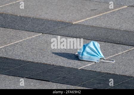 Gebrauchte chirurgische oder medizinische Schutzmaske aufgegeben oder als weggeworfen Müll oder Müll auf dem Boden auf der Straße Stockfoto