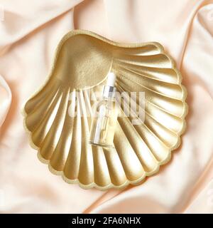 Flasche mit Serum-Lotion für die Gesichtspflege auf goldenem Muschel auf Pfirsichgewebe. Gesichtspflegekonzept. Flach liegend, Draufsicht. Stockfoto
