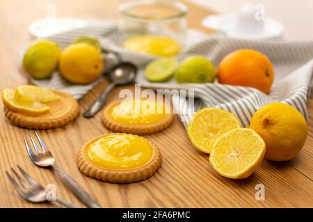 Einige frisch gebackene Plätzchen oder Kuchen mit Zitronenquark, Zutaten auf einem Holztisch wie Zitronen, Orangen, Limetten. Gabeln und Löffel gebrauchsfertig. Stockfoto