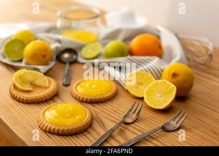 Einige frisch gebackene Plätzchen oder Kuchen mit Zitronenquark, Zutaten auf einem Holztisch wie Zitronen, Orangen, Limetten. Gabeln und Löffel gebrauchsfertig. Stockfoto