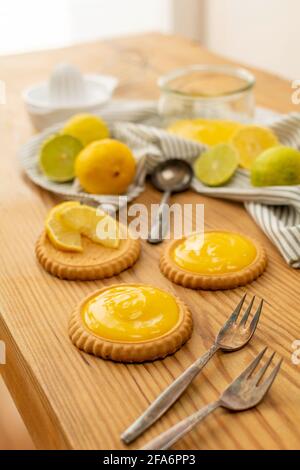 Einige frisch gebackene Plätzchen oder Kuchen mit Zitronenquark, Zutaten auf einem Holztisch wie Zitronen, Orangen, Limetten. Gabeln und Löffel gebrauchsfertig. Stockfoto