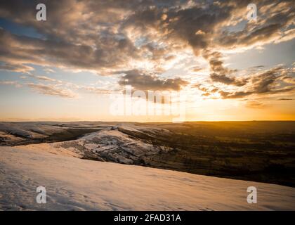 MAM Tor Derbyshire Peak District Bergrücken Wandern im Winter Schneetal und goldorange Sonne, die auf launische Atmosphäre aufgeht Winter schneebedeckten Berg Stockfoto