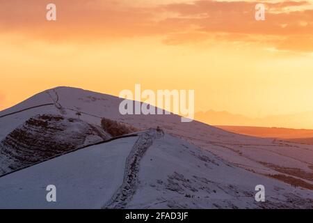 MAM Tor Derbyshire Peak District Bergrücken Wandern im Winter Schneetal und goldorange Sonne, die auf launische Atmosphäre aufgeht Winter schneebedeckten Berg Stockfoto