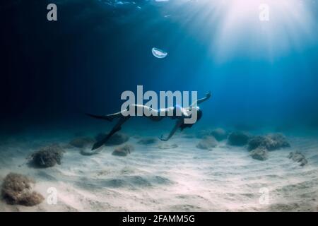 Freitaucher posieren mit Quallen unter Wasser über sandigen Boden im tropischen Ozean. Stockfoto