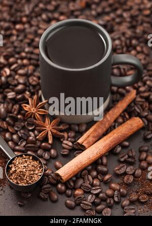 Schwarzer Kaffee in einer hohen Tasse mit Anisstern und Zimt auf gemahlenem Kaffee und Bohnen im Hintergrund mit Kaffeekülze. Stockfoto