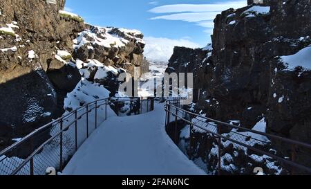 Abnehmende Perspektive des schneebedeckten Wanderweges, der durch die Schlucht Almannagjá im Nationalpark Þingvellir, Island, einem Rifttal, führt. Stockfoto