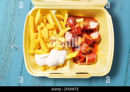 Direkt über der Ansicht von Currywurst und pommes mit Mayonnaise In der Schachtel zum Mitnehmen auf dem Holztisch Stockfoto