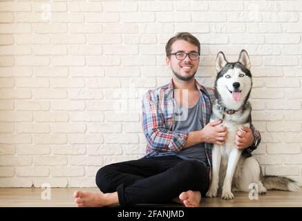 Junger bärtiger Mann, der mit seinem Husky-Hund hinausgehängt hat. Hipster-Mann trägt kariertes Flanell-Shirt und graues Tank-Top verbringen hochwertige Zeit mit vier l Stockfoto