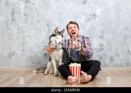 Junger bärtiger Mann, der mit seinem Husky-Hund hinausgehängt hat. Hipster-Mann trägt kariertes Flanell-Shirt und graues Tank-Top verbringen hochwertige Zeit mit vier l Stockfoto