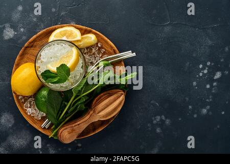 Mojito oder Lemonade Cocktail im Longdrinkglas mit Eiswürfeln, Minze und Limette auf schwarzem Steingrund mit Shaker und Becher. Menüleiste. Platz für Text Stockfoto